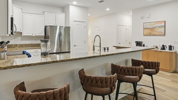 A modern kitchen with white cabinets, a stainless steel refrigerator, a granite countertop, and a bar area with brown upholstered stools. - The Moon Valley Oasis - Spacious 7-bedroom house with Pool, and Game room. (Four Corners)