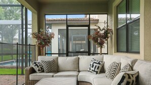 A covered patio area with a sectional sofa and a coffee table, large windows, and potted plants. - The Moon Valley Oasis - Spacious 7-bedroom house with Pool, and Game room. (Four Corners)