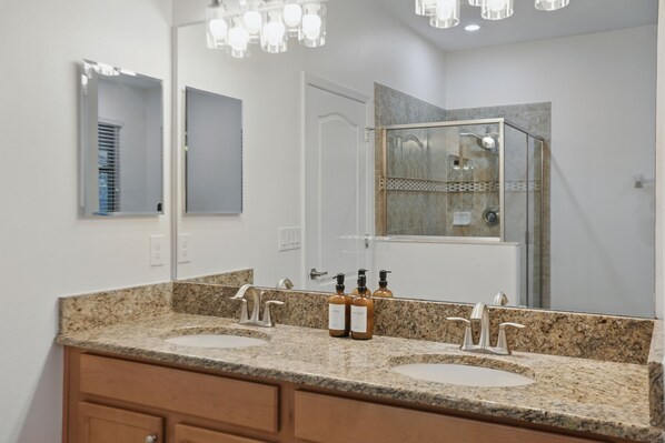 A bathroom with two sinks, a shower, and a large mirror.