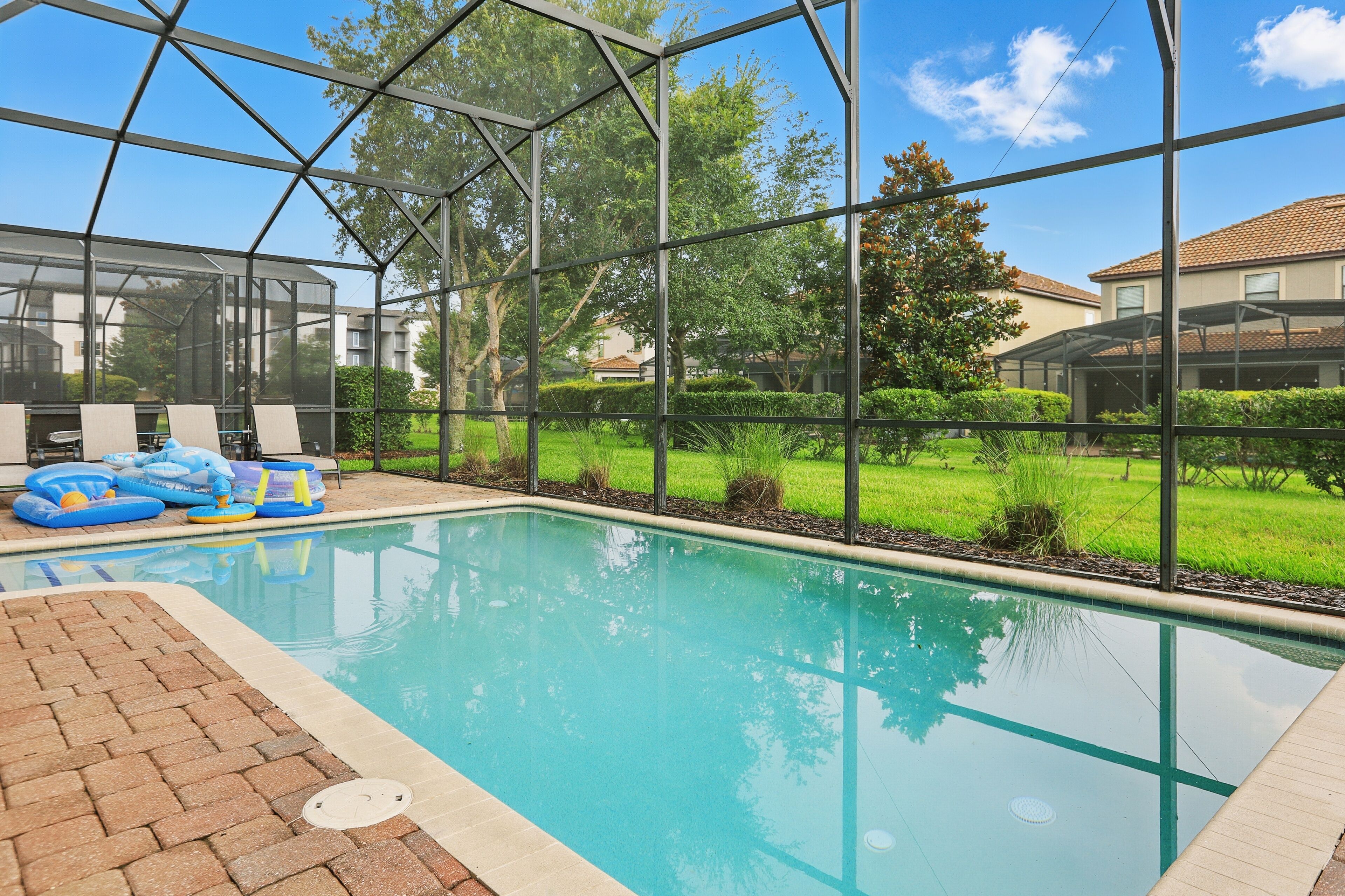 Una piscina con cerramiento de vidrio, rodeada de un patio de ladrillo y abundante vegetación.