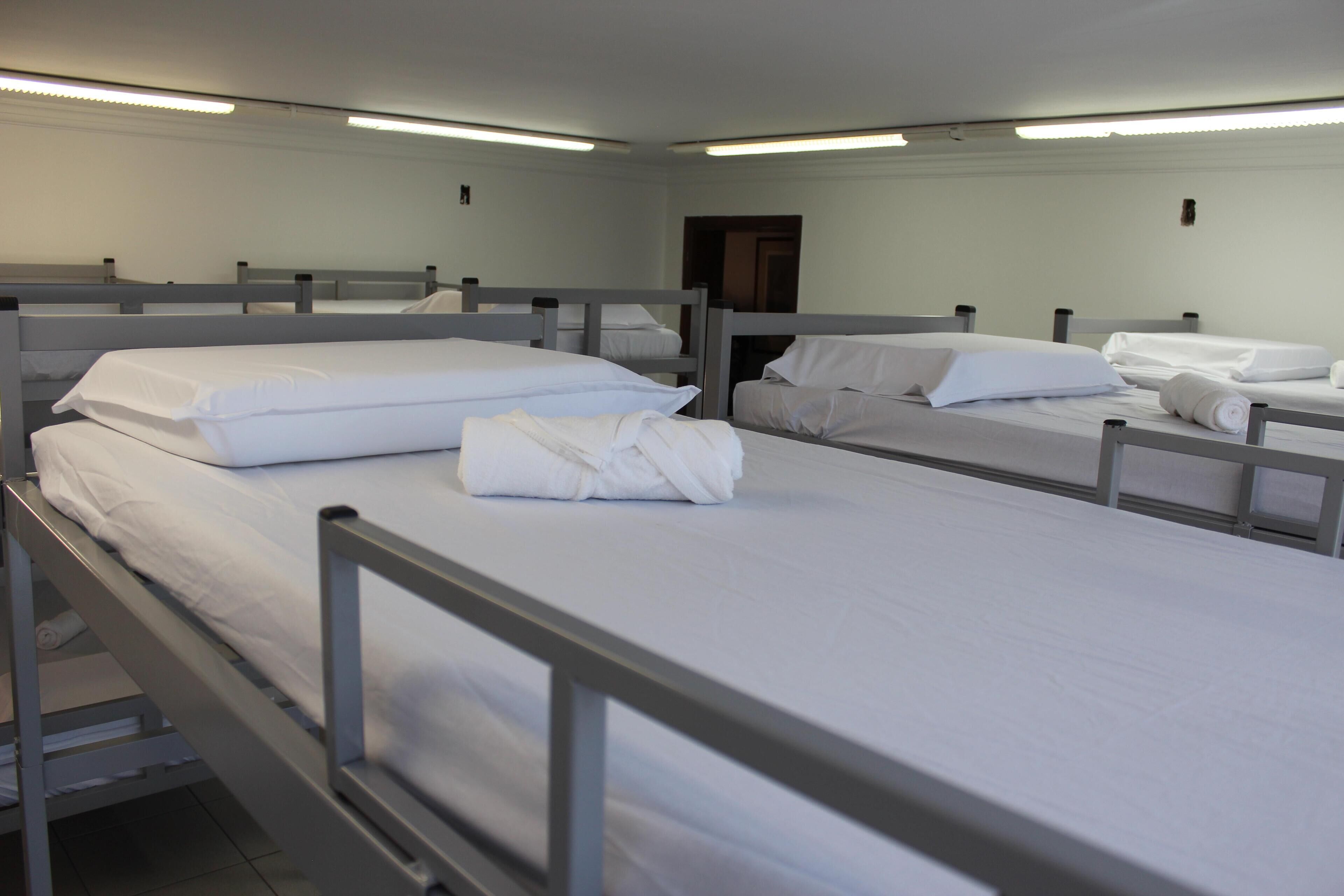 Habitación tipo dormitorio con literas, cada una con ropa blanca y almohadas.