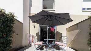 An outdoor patio with a table and two chairs, a large umbrella, and a building in the background.