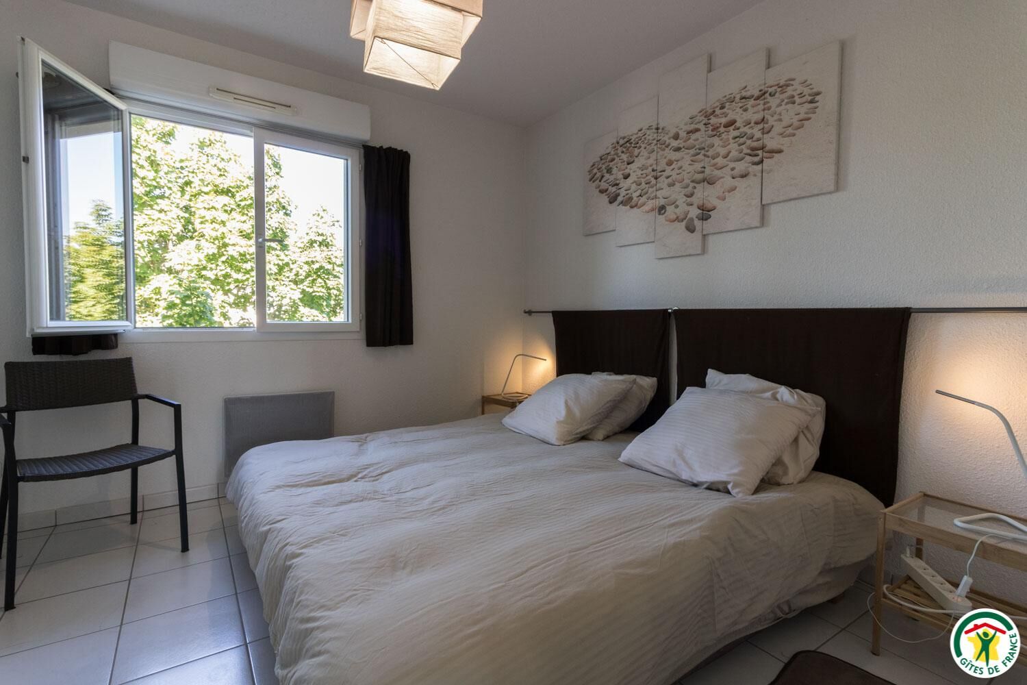 Een slaapkamer met een bed, een stoel, een bureau, een raam en een kunstwerk aan de muur.