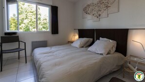 A bedroom with a bed, a chair, a desk, a window, and a wall art piece.