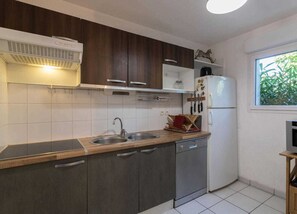 A modern kitchen with dark wooden cabinets, a white refrigerator, and a window with a view of greenery. - Bag End - Gragnague - Gîte (Gragnague)