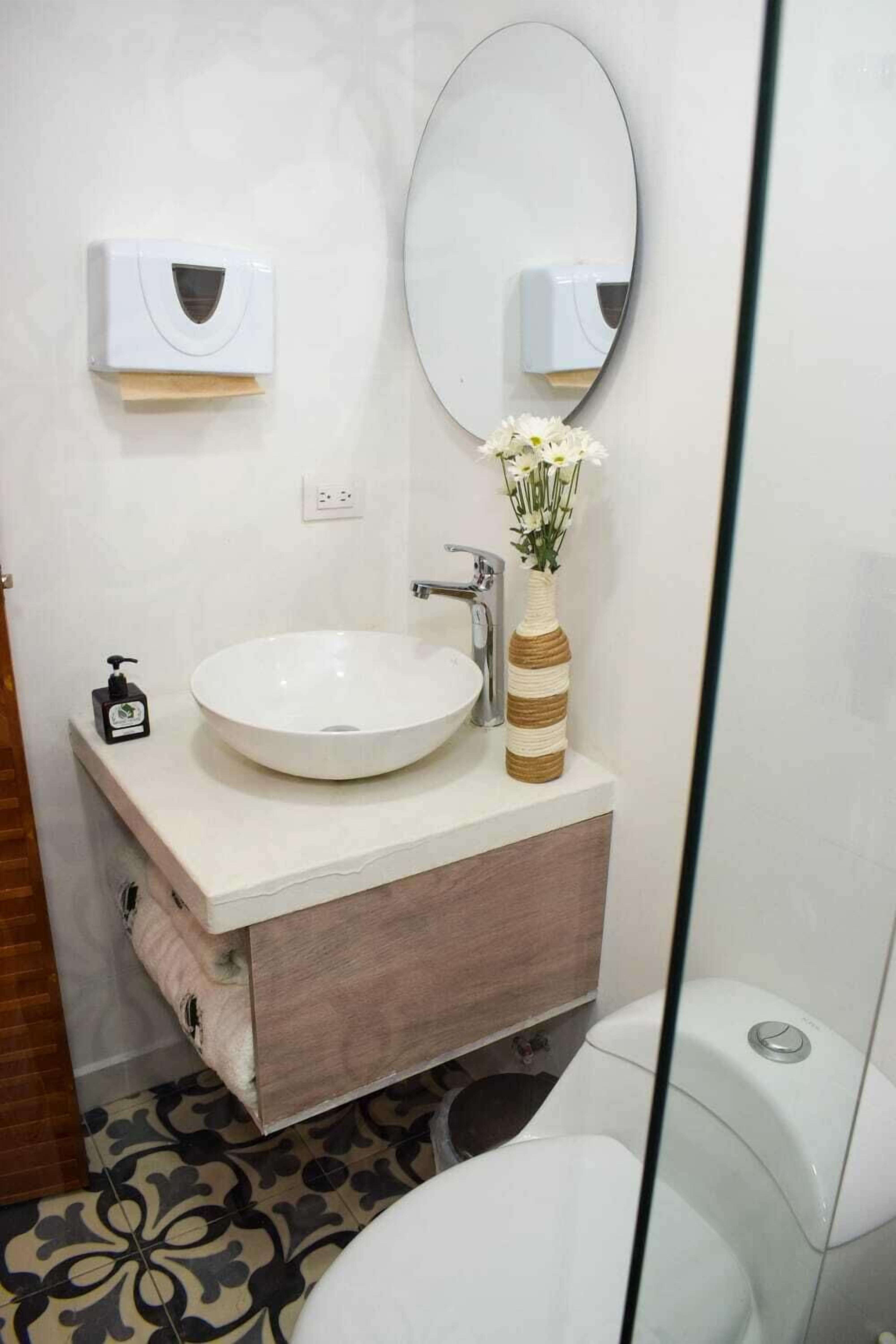 Ein Badezimmer mit Waschbecken, Spiegel, einer gestreiften Vase mit Blumen und Toilette.