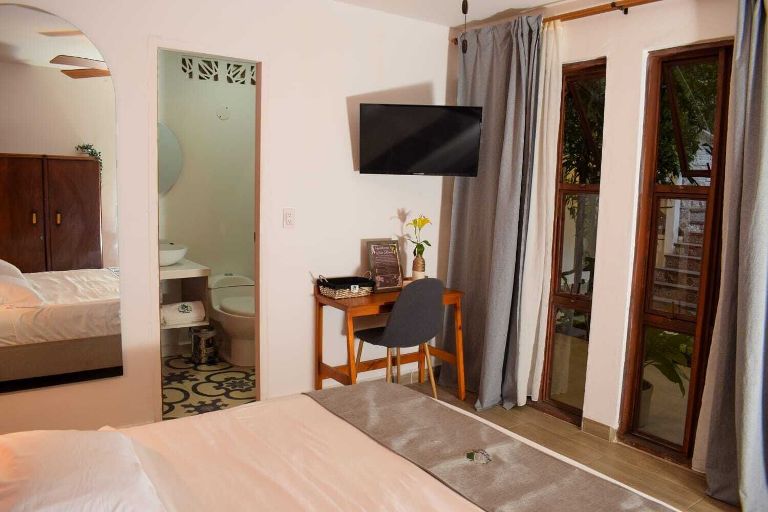 A hotel room with a bed, a desk with a chair, a television, a bathroom, and a sliding glass door to the outside.