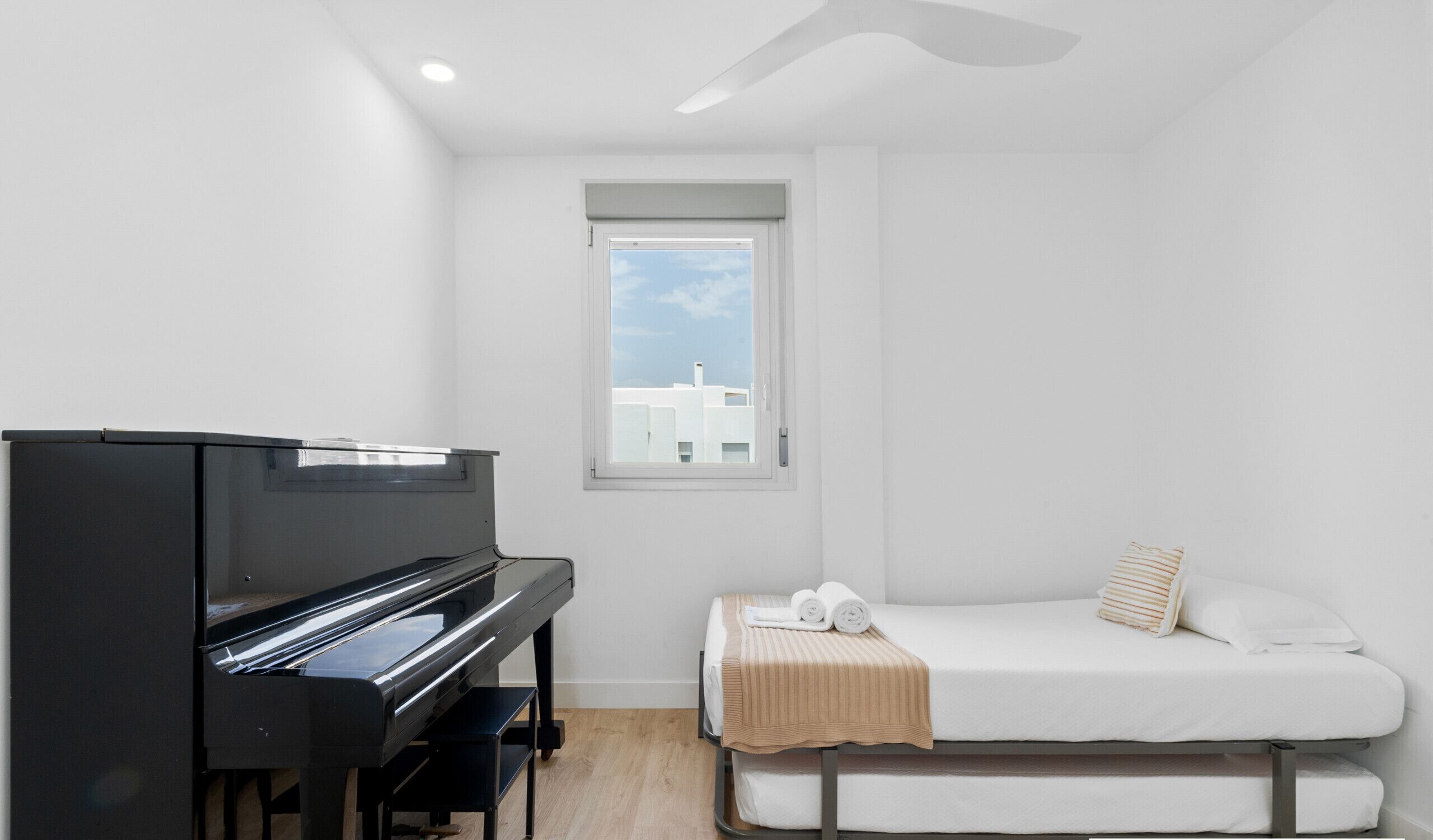 Una habitación pequeña y moderna con un piano, una cama y un ventanal con vistas a edificios.