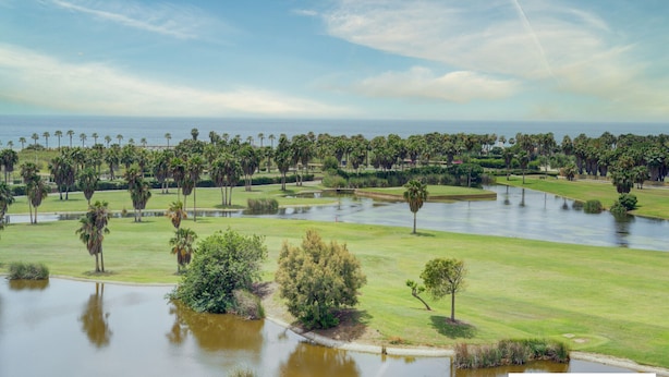 Ein Golfplatz mit Wasserhindernissen, Palmen und Blick auf den Ozean.
