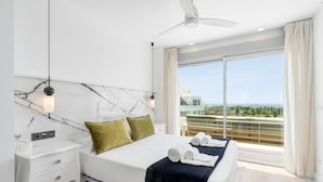 Ein modernes Hotelzimmer mit einem großen Bett, einem Nachttisch, einem Deckenventilator und einem Balkon mit Meerblick.