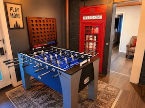 Una mesa de fútbol de mesa en una habitación con una cabina telefónica roja y un letrero que dice 'PLAY MORE'.