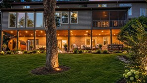 A modern house with a large tree in the front yard, a covered outdoor seating area, and a brick exterior.
