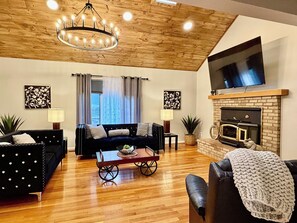 Una sala de estar con chimenea, piso de madera, un sofá, una mesa de centro y un televisor montado en la pared.