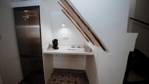 A compact kitchen with a stainless steel refrigerator, a white countertop, and a patterned tile floor.