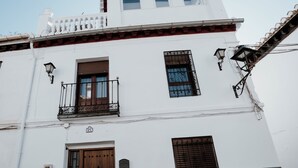 A two-story building with a white facade, a wooden door, and a balcony with a metal railing.