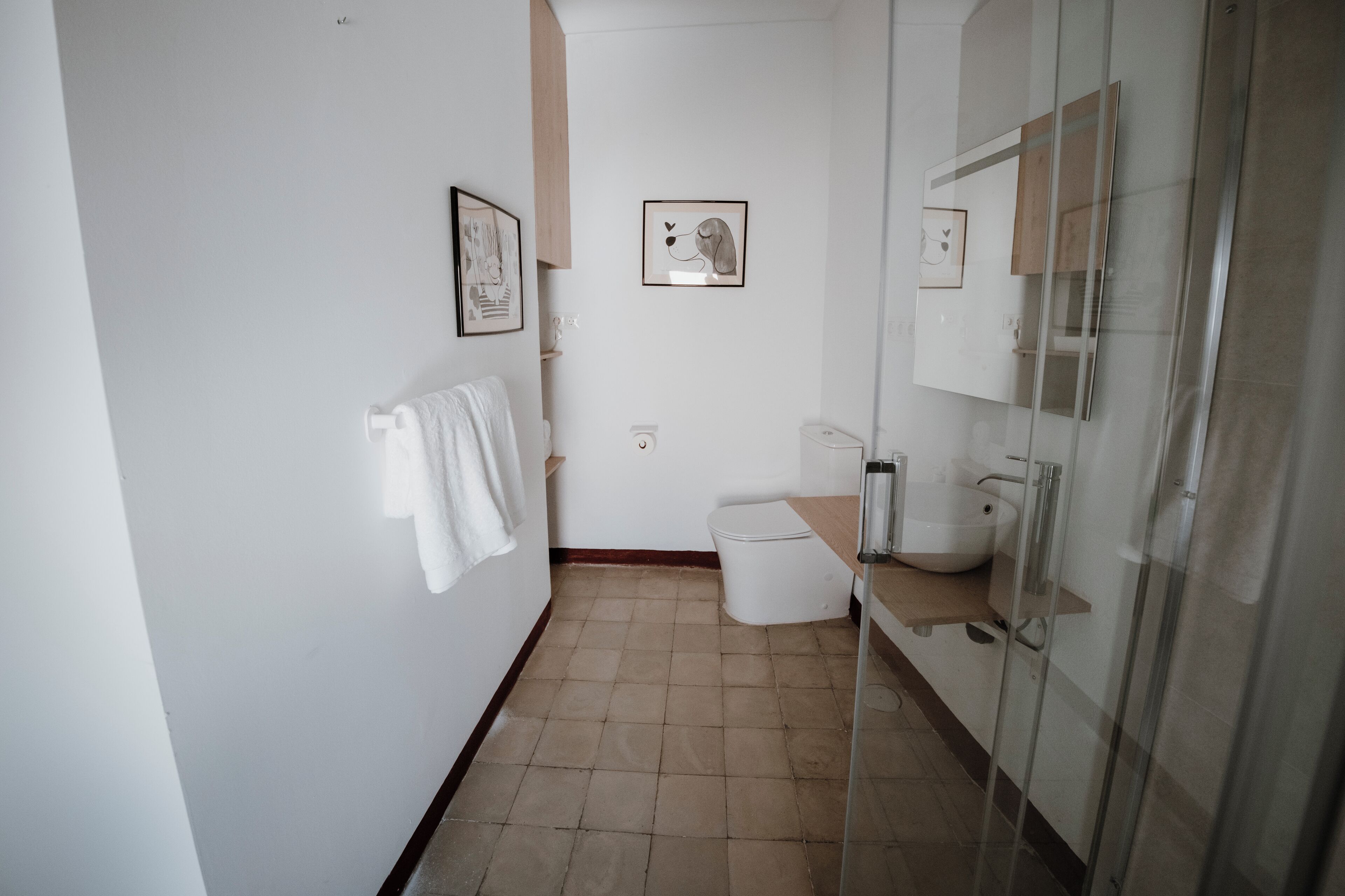 Un baño con inodoro, lavamanos y cabina de ducha de vidrio. Hay cuadros enmarcados en la pared y una toalla colgada.