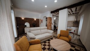 A living room with a sofa, two armchairs, a coffee table, and a checkered floor. There is a kitchen in the background with a stove and a sink.