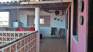 A covered outdoor seating area with a stone floor, a white pillar, and a wall with decorative plates. - Hostel Muiraquitã (Aracati)