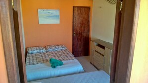 A bedroom with a bed, a wooden door, and a painting on the wall. - Hostel Muiraquitã (Aracati)