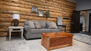 A living room with a grey sofa, a wooden coffee table, and a log wall. - Our beautiful lodge near Albany, MO is sure to please! Perfect for large groups (Albany)