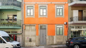 A multi-story building with a red facade, a gated entrance, and a parked car. - VIVA João IV Residence Studios 0F (Porto)