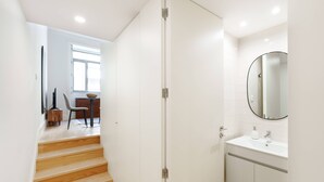 A modern bathroom with a white sink, mirror, and wooden staircase leading to a dining area. - VIVA João IV Residence Studios 0F (Porto)