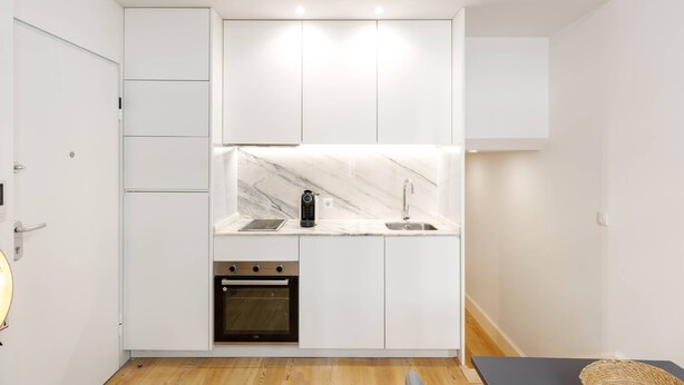 A compact kitchen with white cabinetry, a marble countertop, a built-in oven, and a sink. - VIVA João IV Residence Studios 0F (Porto)