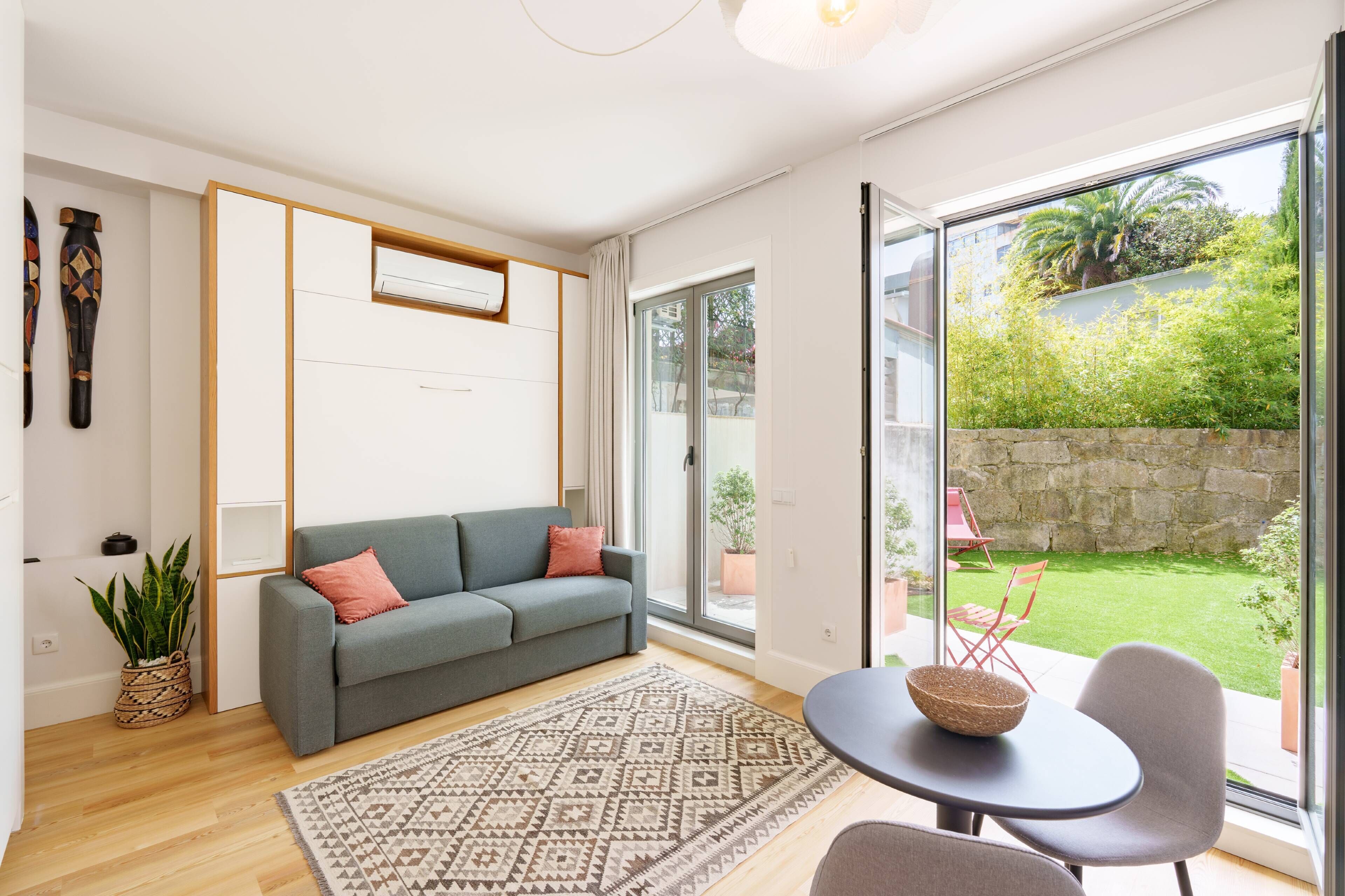 A modern living room with a grey sofa, a patterned rug, and a dining area with a table and chairs.