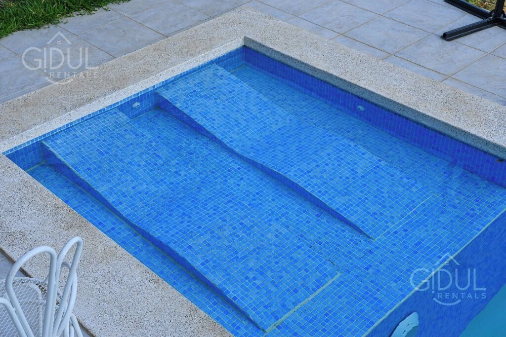A rectangular pool with blue mosaic tiles, surrounded by a stone border.