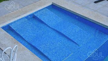 A rectangular pool with blue mosaic tiles, surrounded by a stone border.
