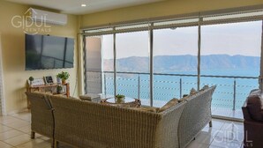 A living room with a sofa, a TV, and a view of the sea. - Stunning Lake-view Villa at Coatepeque - Wifi, A/C (El Congo)