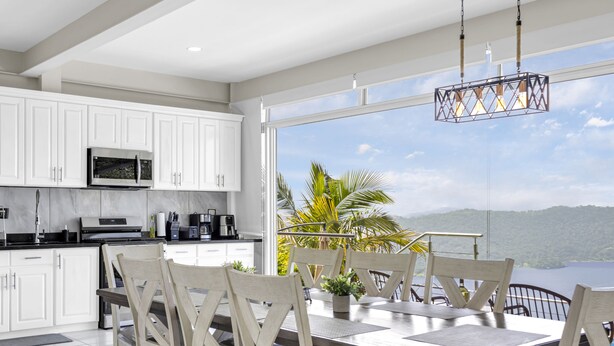 A modern kitchen with white cabinets, stainless steel appliances, and a dining area with a table and chairs. - Stunning Lake-view Villa at Coatepeque - Wifi, A/C (El Congo)