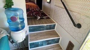 Una escalera estrecha con escalones de madera y un revestimiento mural con patrón hexagonal. Se observa un dispensador de agua a la izquierda.