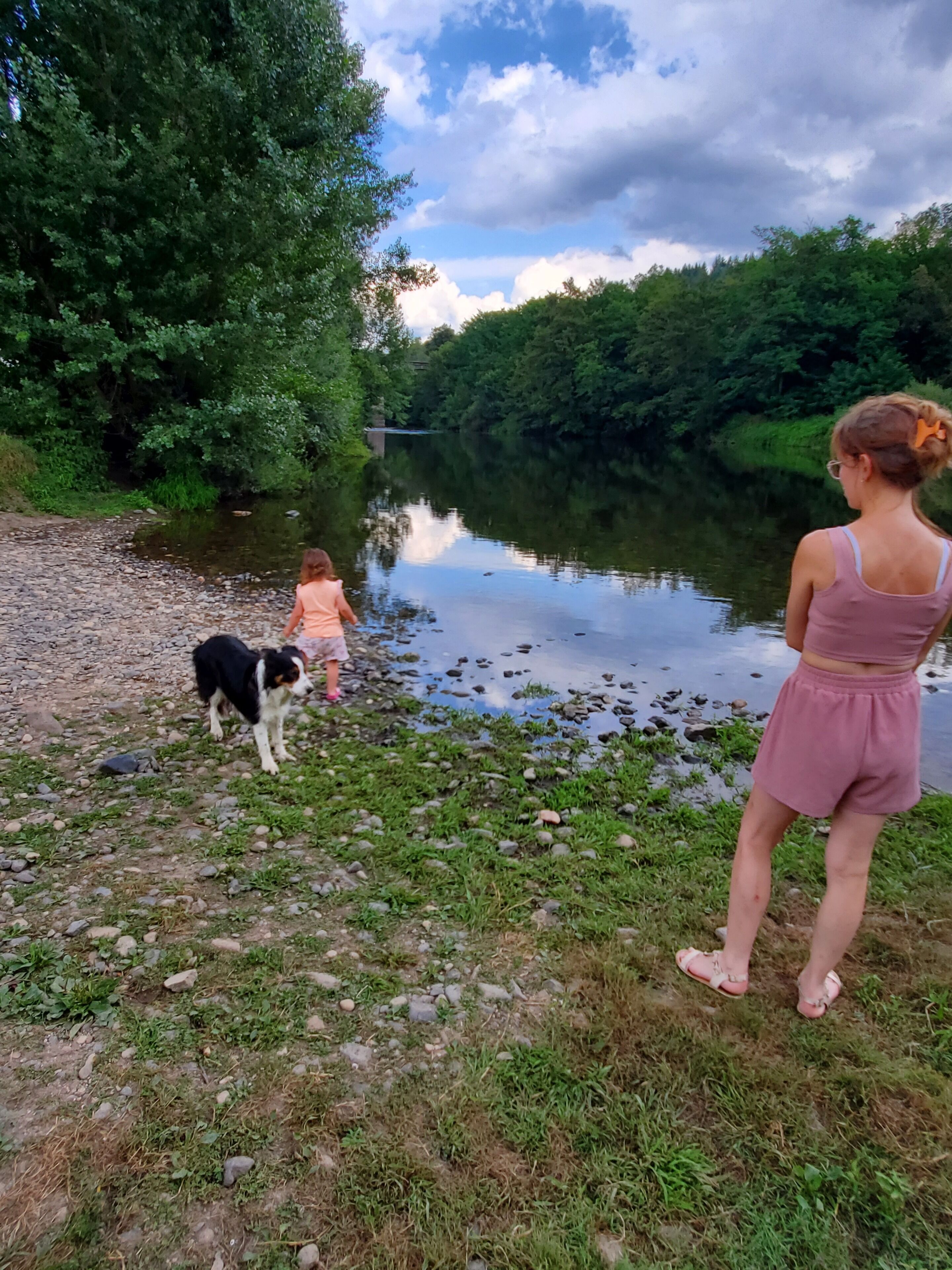 A riverbank with a dog and two people.