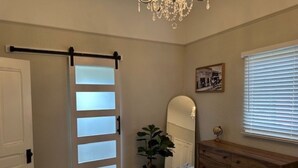 Una camera da letto con un letto, una cassettiera, uno specchio, un lampadario e una porta scorrevole con pannelli di vetro satinato.
