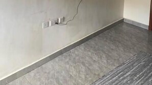 A room with a flat-screen TV mounted on the wall, a power outlet, and a grey tiled floor.