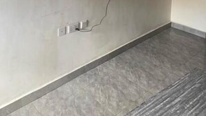 A room with a flat-screen TV mounted on the wall, a power outlet, and a grey tiled floor.