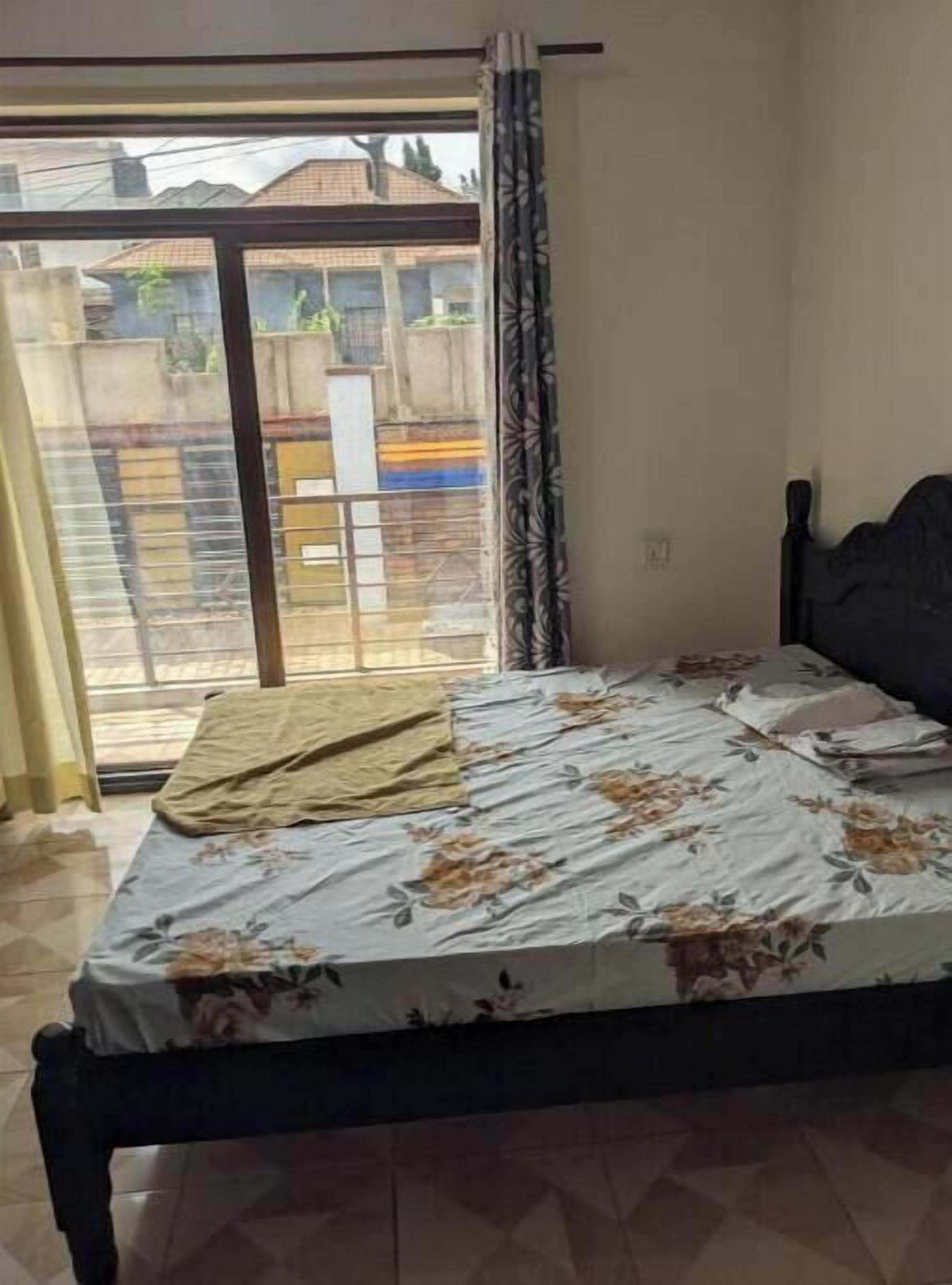 Un dormitorio con cama, ventana con cortinas y vista a una zona residencial.