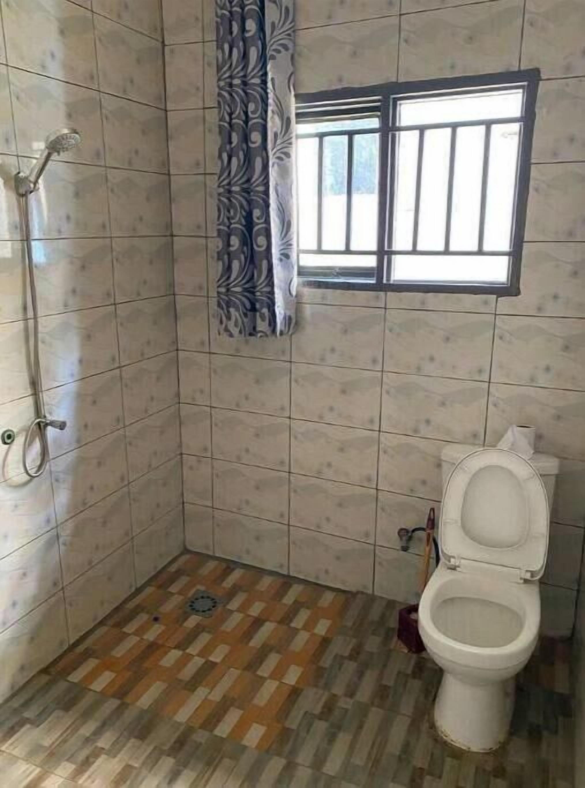 A bathroom with tiled walls, a patterned floor, a shower, a toilet, and a window with bars.