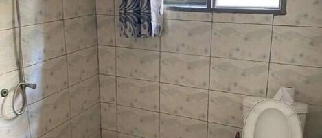 A bathroom with tiled walls, a patterned floor, a shower, a toilet, and a window with bars.
