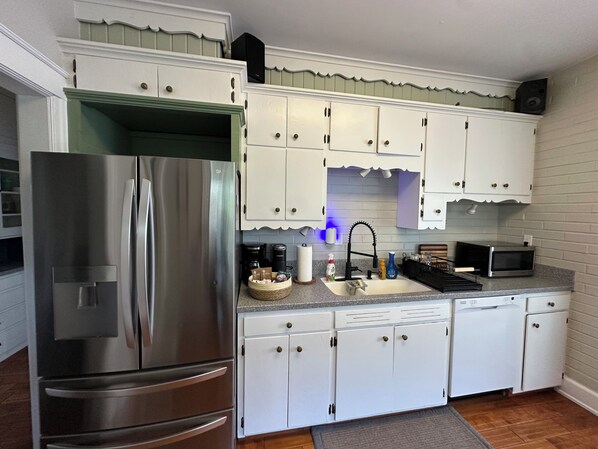 A modern kitchen with white cabinets, a stainless steel refrigerator, a microwave, and a sink.