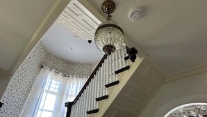 Eine Treppe mit einer Chandelierleuchtre, einer Wand mit Muster und einem Fenster mit Vorhängen.