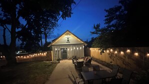Ein Garten mit überdachter Terrasse, Holzzaun und Lichterketten.