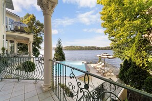 A balcony with a pool, overlooking a body of water and a distant hill.