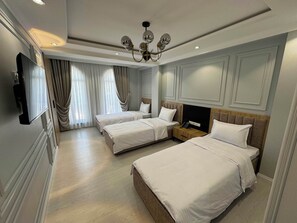 Habitació d'hotel amb dos llits, un televisor, una làmpada de cristall i una tauleta de nit de fusta.