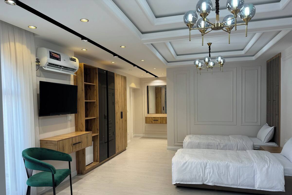A modern bedroom with a large bed, a TV, a wardrobe, and a desk.