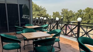 An outdoor patio area with wooden tables and green chairs, a metal railing, and a view of trees and buildings. - Astoria Boutique hotel & SPA (Samarkand)