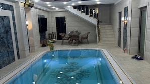 An indoor swimming pool with a hot tub, a dining area, and a staircase leading to upper floors. - Astoria Boutique hotel & SPA (Samarkand)