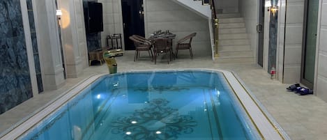 An indoor swimming pool with a hot tub, a dining area, and a staircase leading to upper floors.