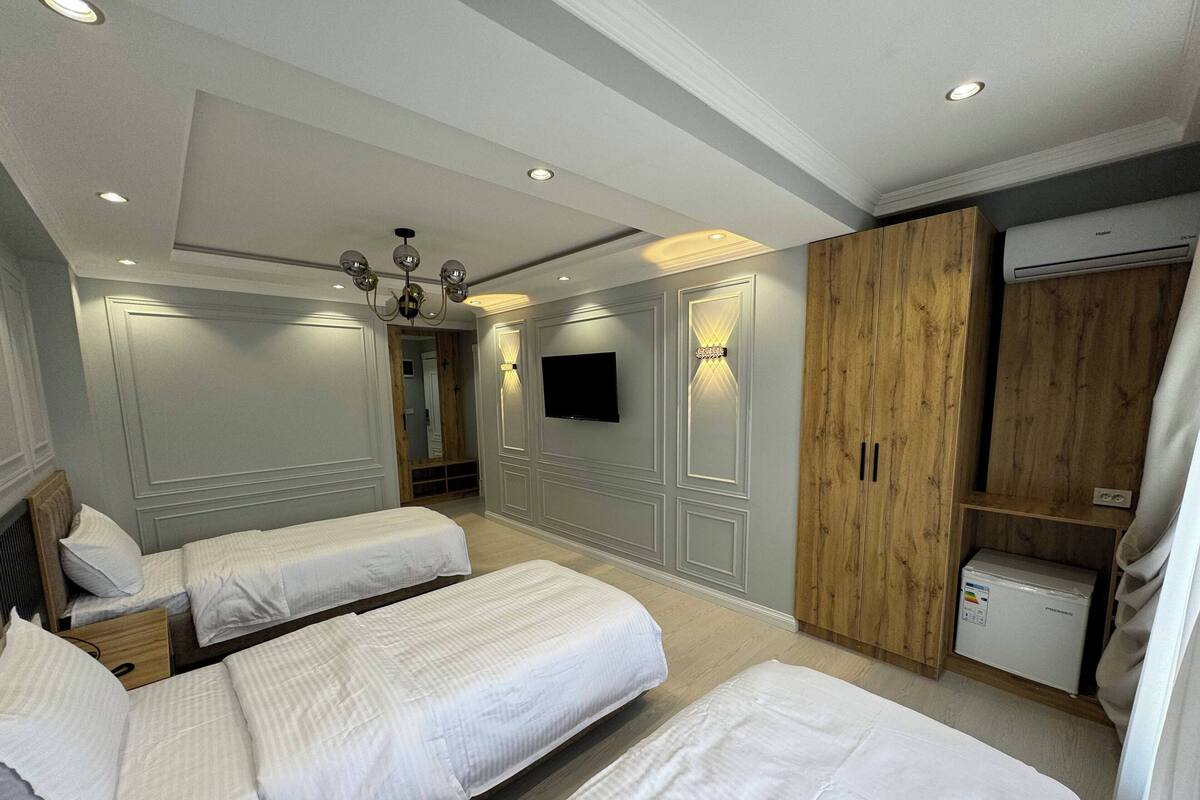 A hotel room with two beds, a television, a wooden wardrobe, and a small refrigerator.